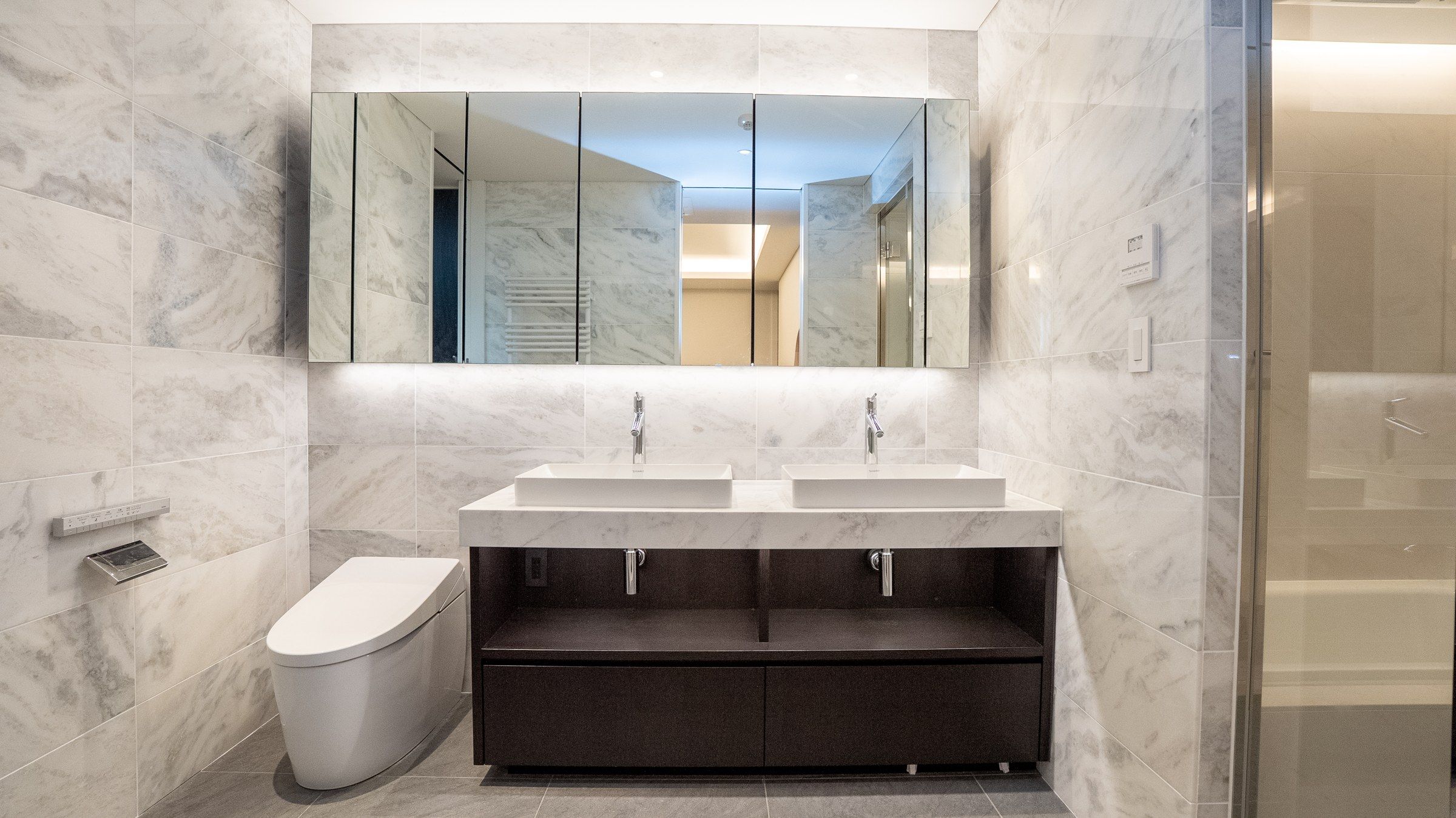 The main bath in grey marble: twin basins beneath a mirrored wall, the shower behind glass.