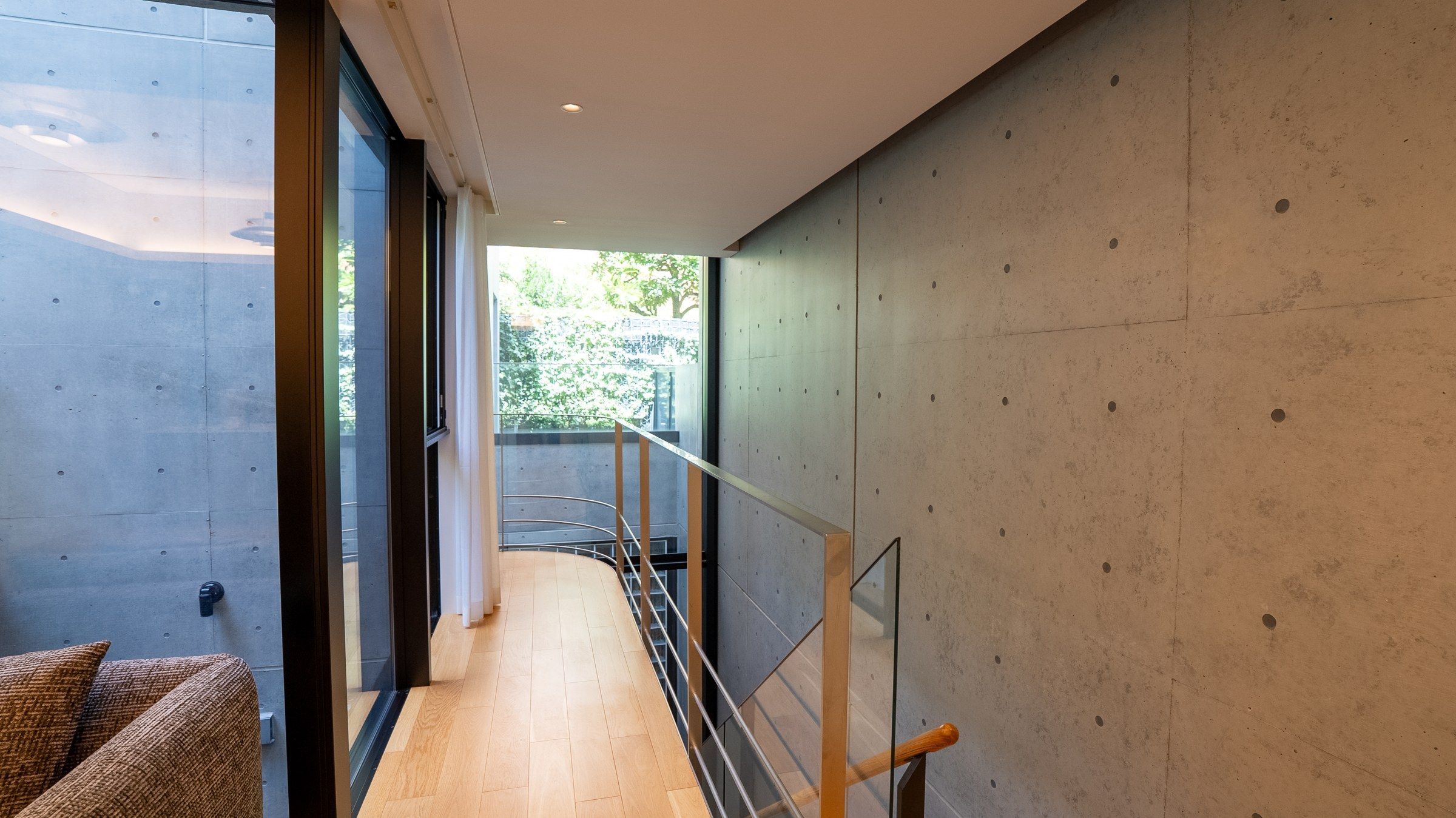 The upper landing: a corridor of oak and glass along the board-marked concrete, the garden's light at its end.