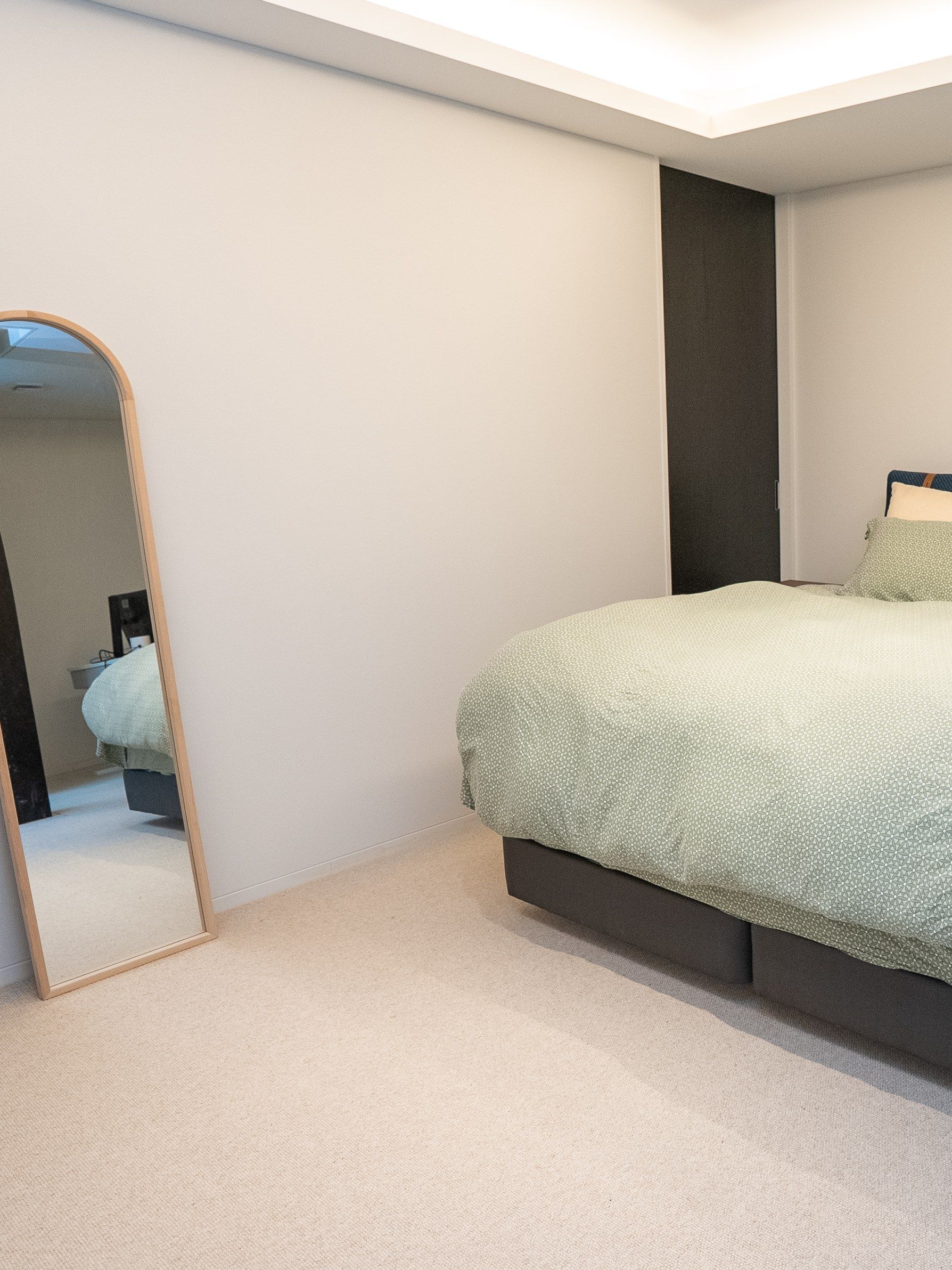 The principal bedroom: a low bed, an arched mirror, carpet underfoot.